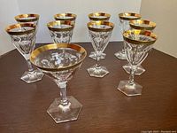 Nine Moser crystal wine glasses arranged on table, front view showing hexagonal stems and gold rims