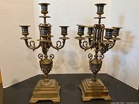 Both brass cloisonné candelabras side by side on black surface with white backdrop