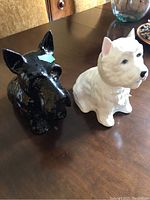 Photo showing both dog-shaped liquor bottles on a wooden table, black and white ceramic bottles in dog head shapes.