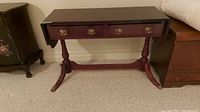 Front view of wood console table showing two drawers, drop-down ends, and turned legs with brass claw feet.