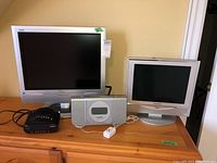 Two Panasonic Viera televisions on a wooden dresser along with a Sony radio alarm clock and a Capello CD alarm clock.