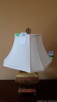 Metal table lamp with a gold-tone base and white fabric lampshade, front view showing base detail and shade shape.