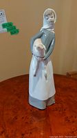 Full view of the Lladro figurine showing the lady holding the lamb standing on a wooden surface.
