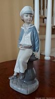 Front view of the Lladro figurine showing the boy sitting holding a sailboat, wearing a blue sailor top and white pants.