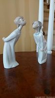 Pair of Lladro boy and girl porcelain figurines facing each other on wooden surface with staircase background.
