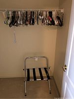 Folding luggage rack positioned in an empty closet under a wire shelving rod with clothes hangers.