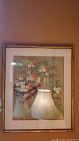Framed art print showing an Asian-style floral bouquet with white and pink flowers, glass glare visible reflecting a lamp.