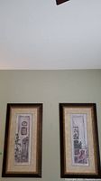 Two framed vertical prints hung side by side on a pale green wall, showing art details and frames