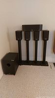 All six speakers and four stands arranged against wall; subwoofer at left, center channel atop two satellites, four satellite speakers on stands