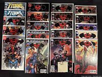 Photo of twenty DC Comics comic books bagged and boarded featuring Titans, Batman, Superman, Supergirl, and Wonder Woman, arranged in rows with clear covers and vibrant artwork.