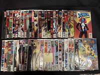 Overhead photo showing 50 comic books arranged in two rows on a black surface. Covers include various titles with characters such as X-Men and Batman.