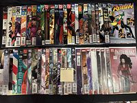 Photo of approximately 50 comic books arranged in two rows showing front covers, diverse titles including Robin, Anita Blake, Teen Titans, and other superhero and fantasy series. Comics mostly bagged individually or in plastic protectors.
