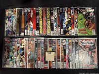 Image showing entire lot of 50 comic books arranged in two rows, colorful superhero themed covers visible with various series names such as 'Code of Honor,' 'Batman,' 'Detective Comics,' and 'Gotham'.