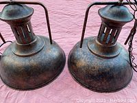 Two vintage industrial barn pendant lamps on a pink background showing dome-shaped shades with rust textured finish and vented tops