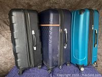 Three large hard shell suitcases in black, navy blue, and bright blue colors side by side on a fabric surface