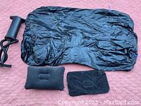 Black inflatable air car bed, two pillows, and black storage pouch, laid out on a pinkish surface.
