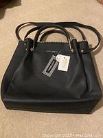 Full front view of the black Alexis Bendel vegan leather tote handbag showing shape, handles, branding, and tags.