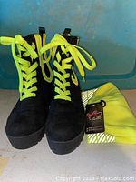 Front view of black boots with neon yellow laces and folded neon yellow beanie hat, both displayed on a surface.