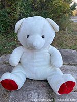 Front view of the life-size white teddy bear with red paw soles, showing its sitting posture, plush fur, and facial features