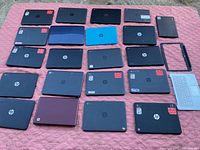 Top-down view of 19 laptops laid out showing black HP models, blue and purple laptops, and detached white keyboard and bezel frame