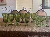 Lot of 17 vintage green glass goblets and stemmed glasses arranged on a table, grouped by size and style, showing front view of the glasses.