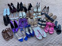 Lot of women's shoes in various styles and colors laid out on a fabric surface.