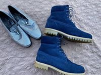 Two pairs of men's shoes including blue suede boots and silver formal loafers shown side by side on a quilted surface.