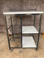 Front side view of metal kitchen island showing two white shelves on right and two wire basket drawers on left. Metal frame and caster wheels are visible.