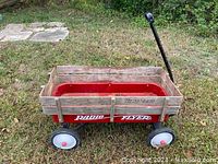 Photo of full Radio Flyer wagon showing red metal bed, wooden sides, black handle, and wheels on grass outdoors.