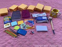 Full overview of the lot on a pink quilted surface showing multiple stacks of manila envelopes, colored stationery and office supplies laid out