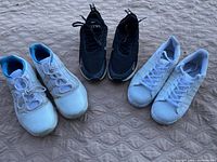 Three pairs of sneakers arranged side by side on carpeted surface: white with blue interior, black with white soles, and white Adidas with three stripes.