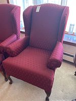 Full view of Bassett upholstered wingback chair showing deep red diamond patterned fabric, winged back, rolled arms, and dark wooden cabriole legs.