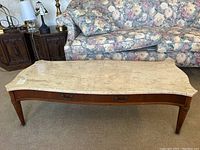 Full view of the rectangular coffee table with stone top and wooden base in front of a floral patterned sofa.