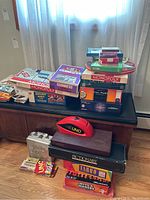 Photo of multiple boxed board and card games stacked on a black table including Monopoly, UNO, Scrabble, Pictionary, and vintage Guinness card game