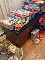 Wooden Lane storage chest with stacked board games and boxed card games on top. Chest has a black padded top and dark wood finish.