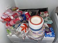 Wide view of lot showing stacked red and blue disposable party cups, stacks of paper plates with various designs, packages of plastic flatware, and holiday-themed paper napkins.