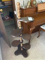 Full view of the wooden plant stand showing multiple tiers with kidney-shaped shelves and central turned wooden spindle column. Dark wood surface with some scratches visible.