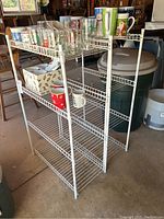 Image of two white metal wire shelves placed in a garage environment with various mugs, glasses, and boxes stored on them.