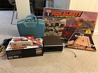 Wide shot showing all items in the lot including boxed toy truck set, boxed musical instrument, boxed massager, small blue carrying case, black 8 track player and aerobic bells box.