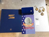 Lot items on table including blue stamp album, 50 States Quarters album, blue coin holder, and gold commemorative medallions