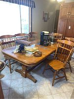 Full view of the wooden dining table with six matching chairs around it, table top crowded with various items.