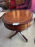 Front view of round wooden table with leather inlay top, showing wear