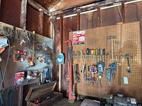 Wide view showing pegboards with assortment of hand tools including wrenches, saws, clamps, hammer, and screwdrivers hung on wall.