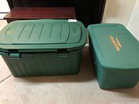 Four green plastic storage bins with lids of varying sizes, showing the larger bin with ribbed lid and latches