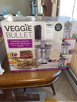 Front view of the Veggie Bullet box showing the product and listing its 3 functions: shred, slice, and spiralize. Box shows food images and product image.