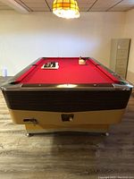 Full length front view of the vintage pool table showing red felt, wooden trim and metal corners, beige base, and metal legs.
