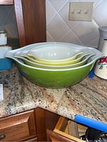 Four nested vintage Pyrex mixing bowls stacked inside each other showing size gradient and green to white color contrast.