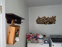 Wooden bag storage box with bear motif hanging from a wall shelf above washing machine, aluminum wall art mounted on wall near shelf.