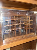 Front view showing the full wooden rolling ball clock inside a clear acrylic case, with visible numbered wooden tracks and metal balls positioned on the first track.