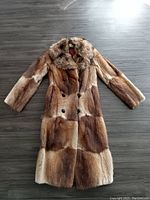 Full coat laid flat on floor showing overall shape, fur quality, and double-breasted button closure.